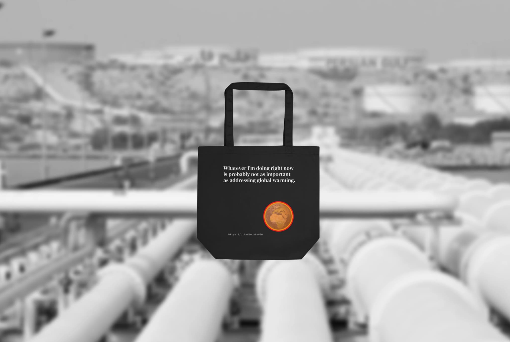 Climate Studio tote bag with global warming message against oil pipeline background